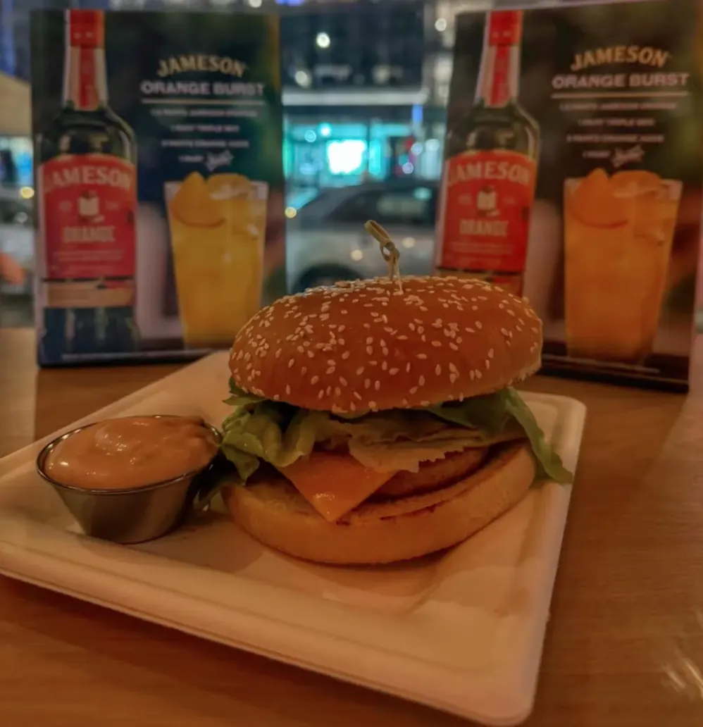 Burger and dipping sauce on a paper plate at the Classic, Jameson Orange promo cards behind